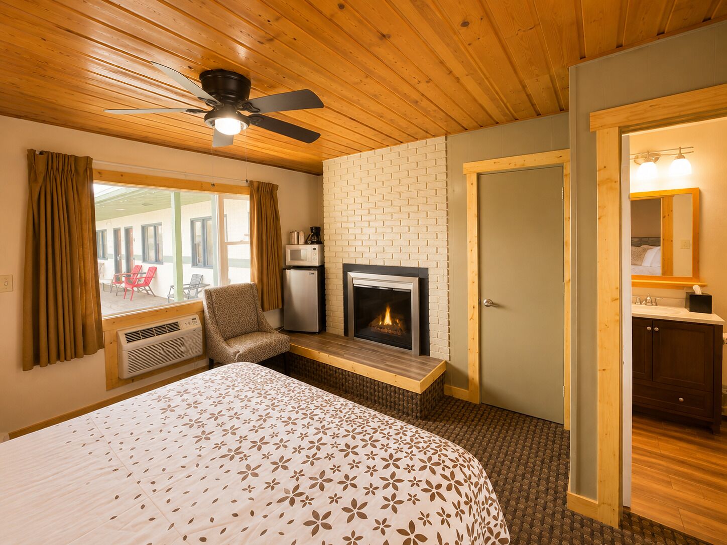 A bedroom with a bed, a fireplace, a ceiling fan, and a view of the outside.