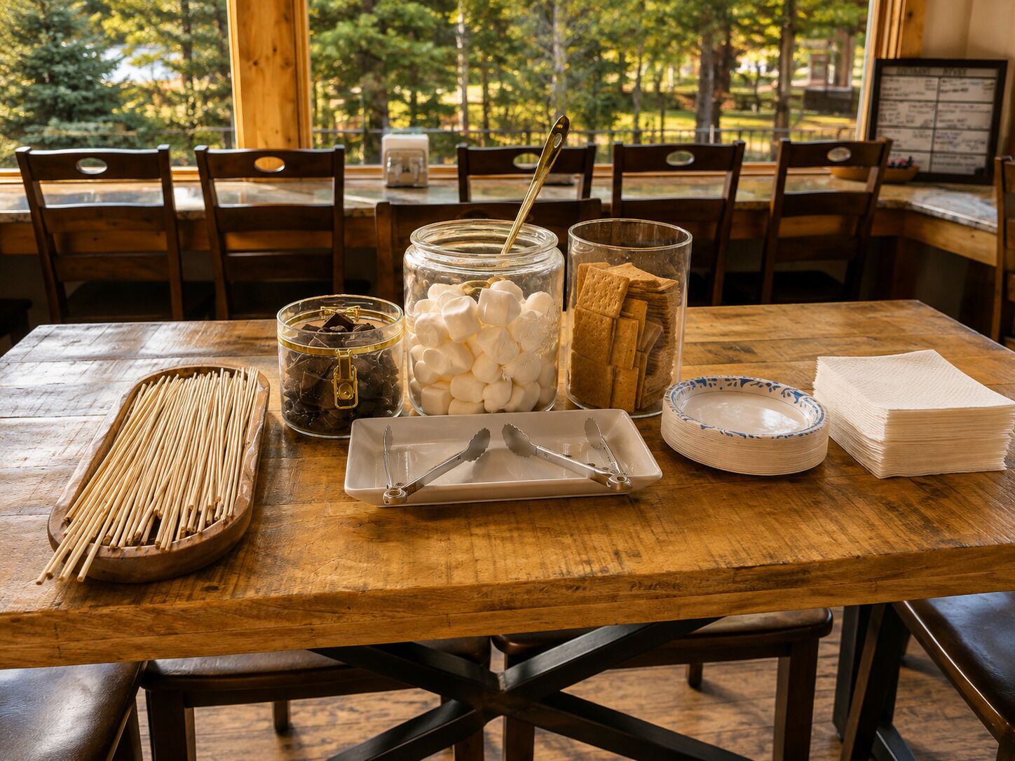 A wooden dining table with various food items and utensils, surrounded by chairs.