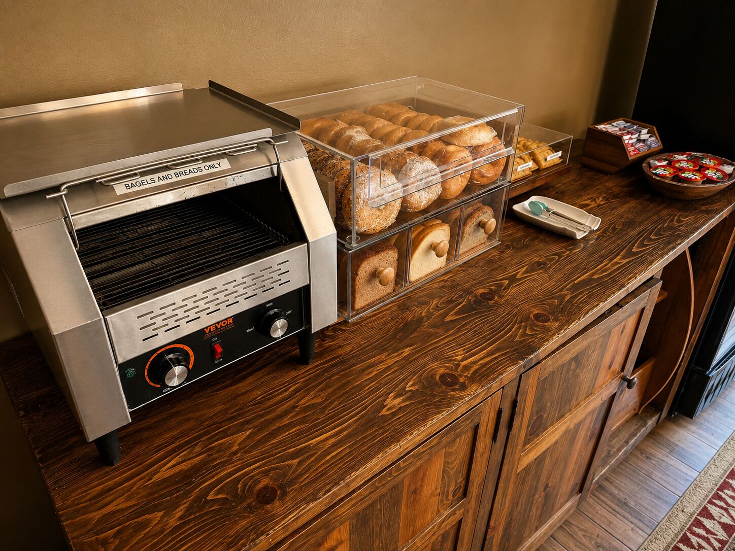 A bread and bagel station with a toaster and a display case containing various breads and bagels.