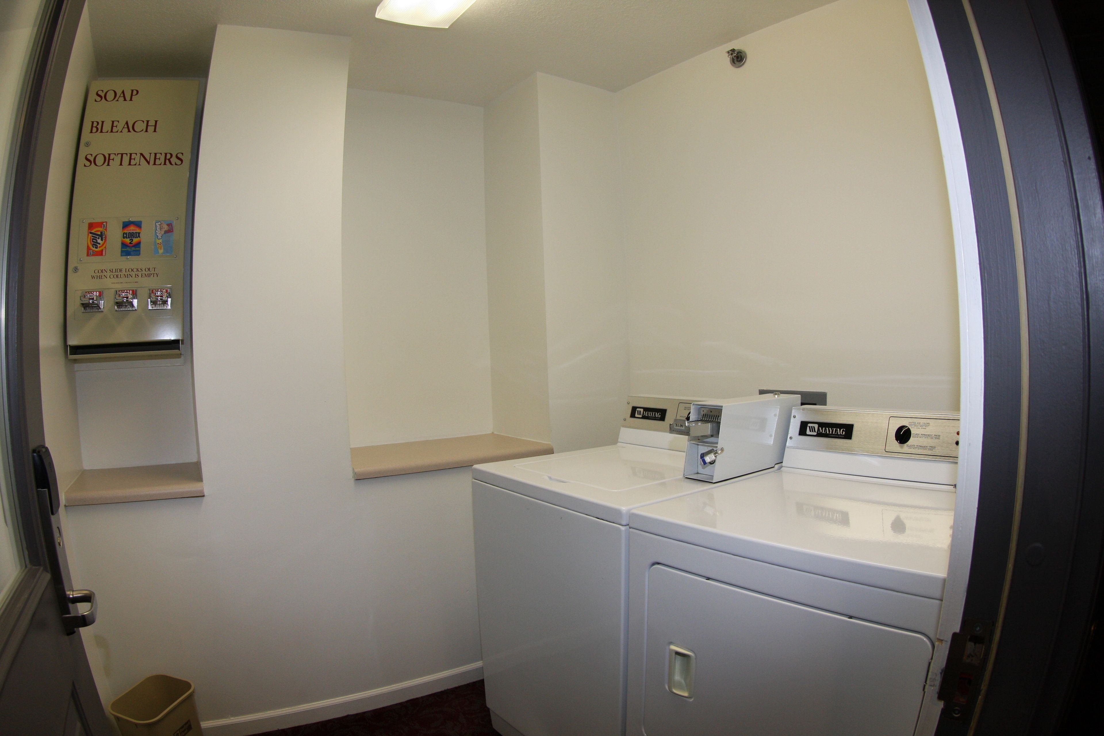 A laundry room with a washer and dryer, a shelf with soap and bleach, and a trash bin.