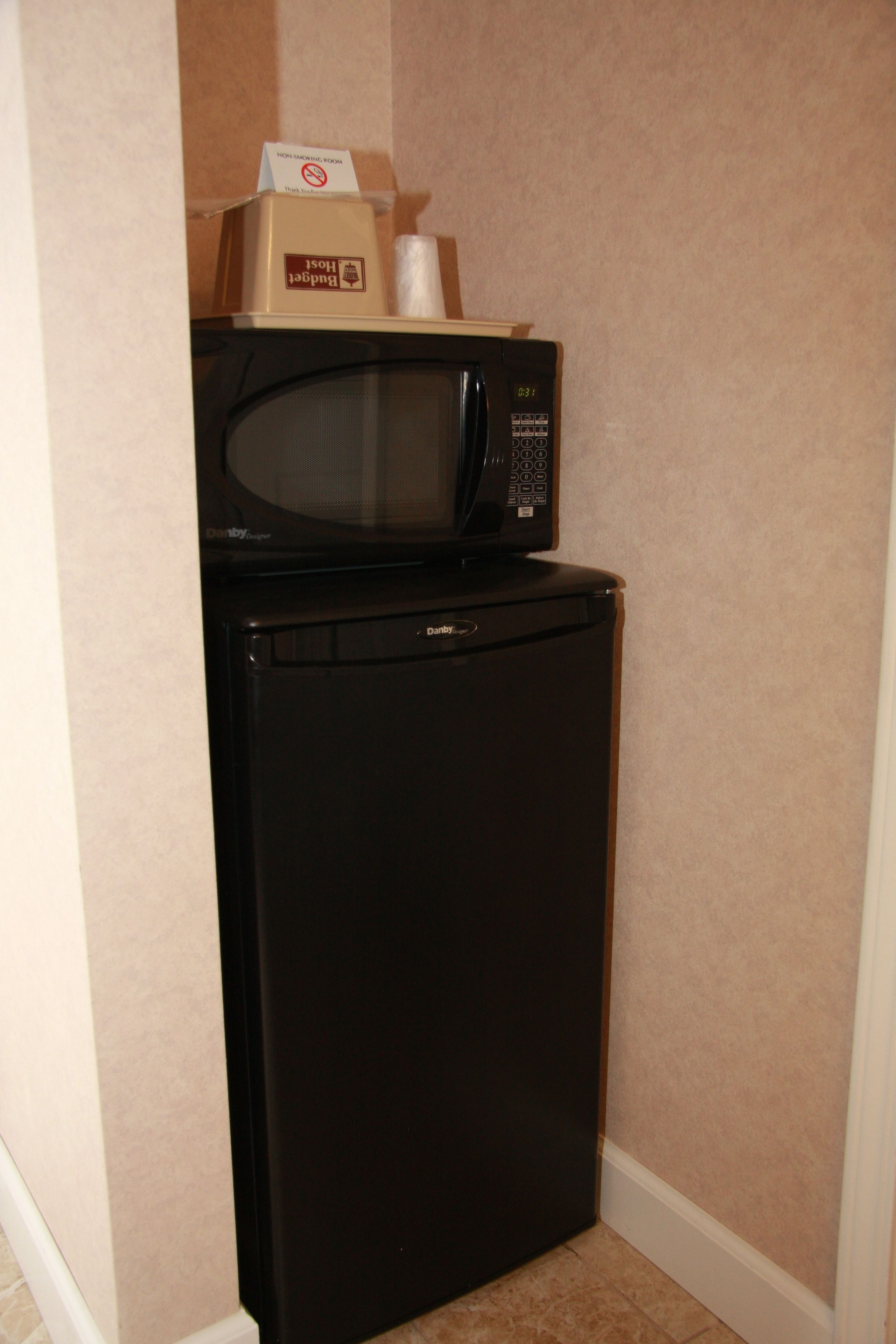 Un refrigerador y microondas negros compactos ubicados en un rincón, con paredes color beige y un zócalo blanco.