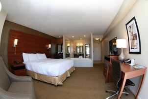 Habitación de hotel con una cama grande, un escritorio con una silla, una lámpara de escritorio, un teléfono y un espejo.