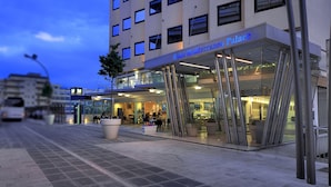 Un hotel con fachada de vidrio moderna, zona de estar al aire libre y entrada visible.