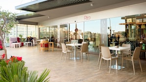 Un café con mesas y sillas, una cafetería al fondo y ventanas amplias.