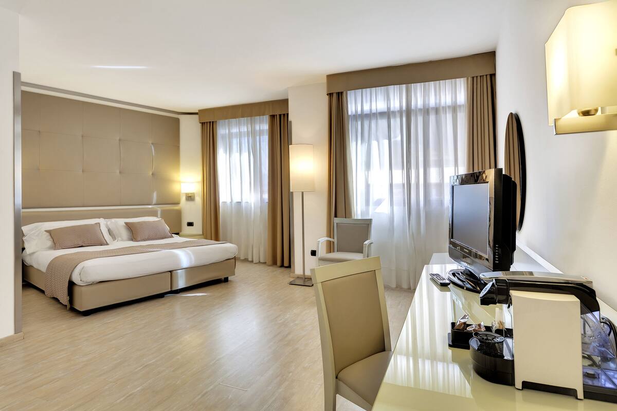 A hotel room with a bed, a desk with a television, a chair, and a lamp.