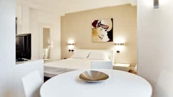 Una habitación de hotel con cama, lámparas de noche, televisión y una mesa de comedor con un bol.