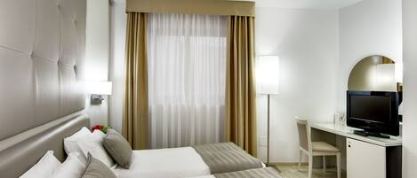 Habitación de hotel con cama, escritorio, televisor y lámpara.