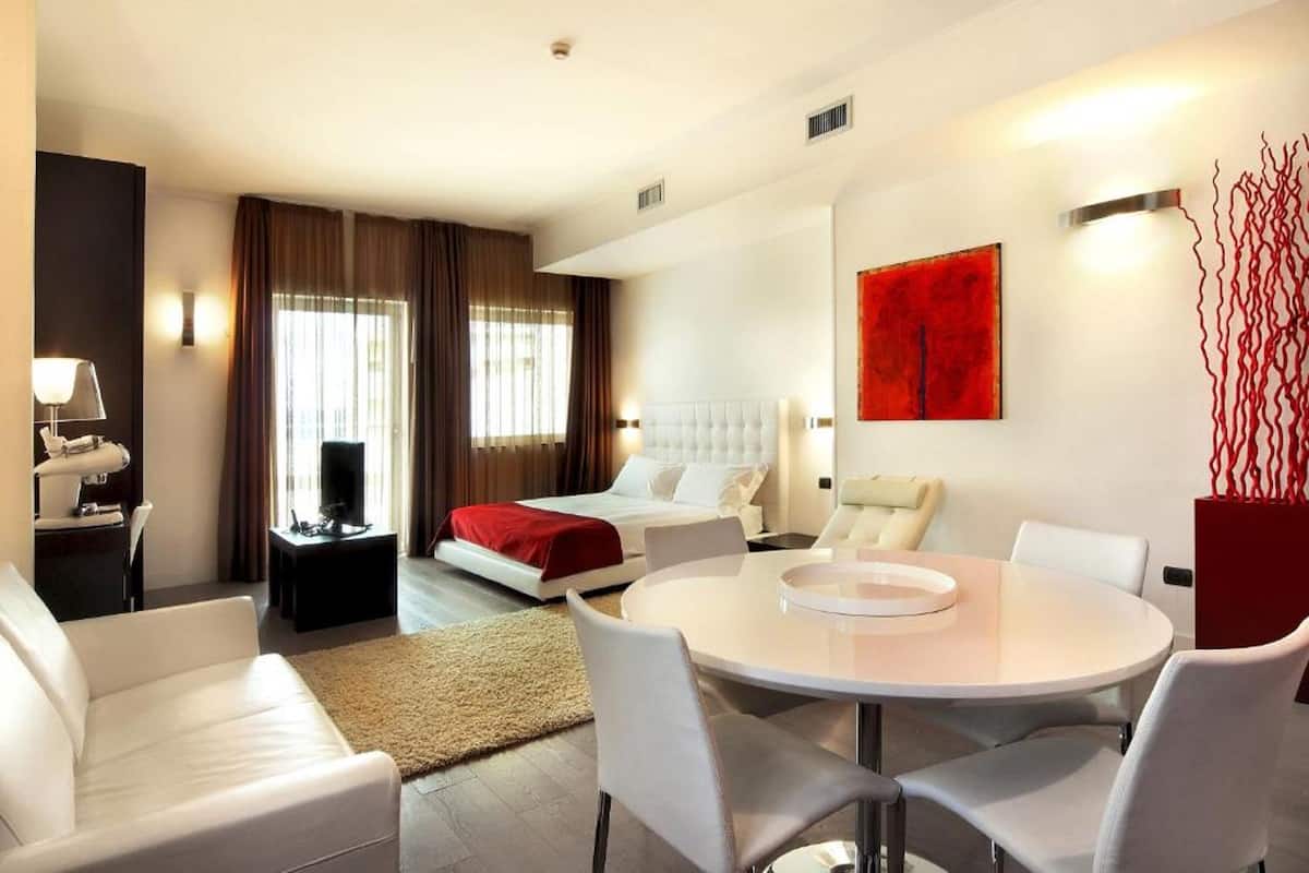 Una habitación de hotel moderna con cama, una mesa de comedor redonda, un sofá y televisor.