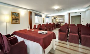 Un salón de conferencias con una larga mesa, filas de sillas, un proyector y un cuadro en la pared.