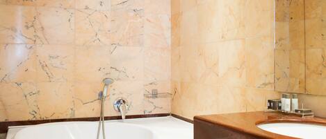 A modern bathroom with a freestanding bathtub, a vanity with a mirror, and marble walls.