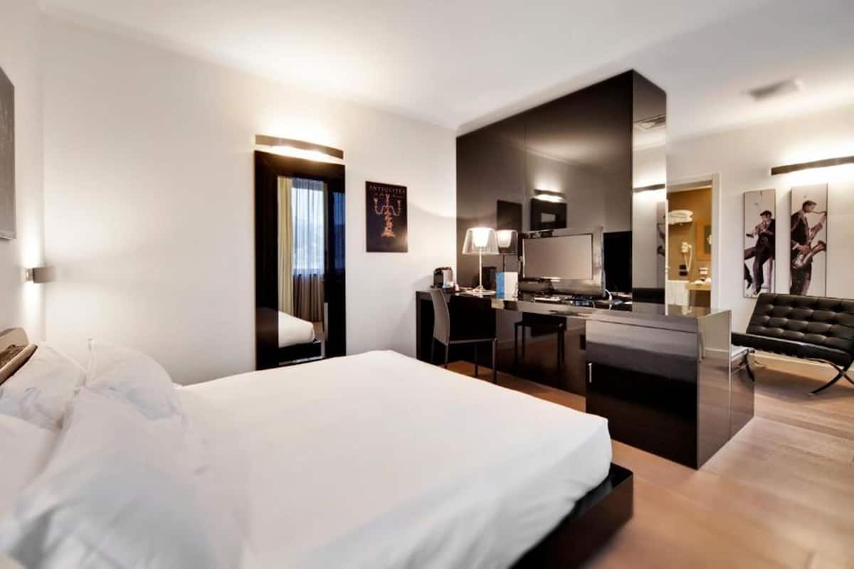 A modern hotel room with a large bed, a kitchenette, a desk, and a seating area.