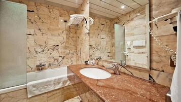 A bathroom with a marble wall, a bathtub, a sink, and a large mirror.
