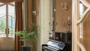 A grand piano in a spacious room with a potted plant, a bench, and elegant wall sconces.