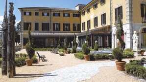 A courtyard with a yellow building, outdoor seating, and statues.