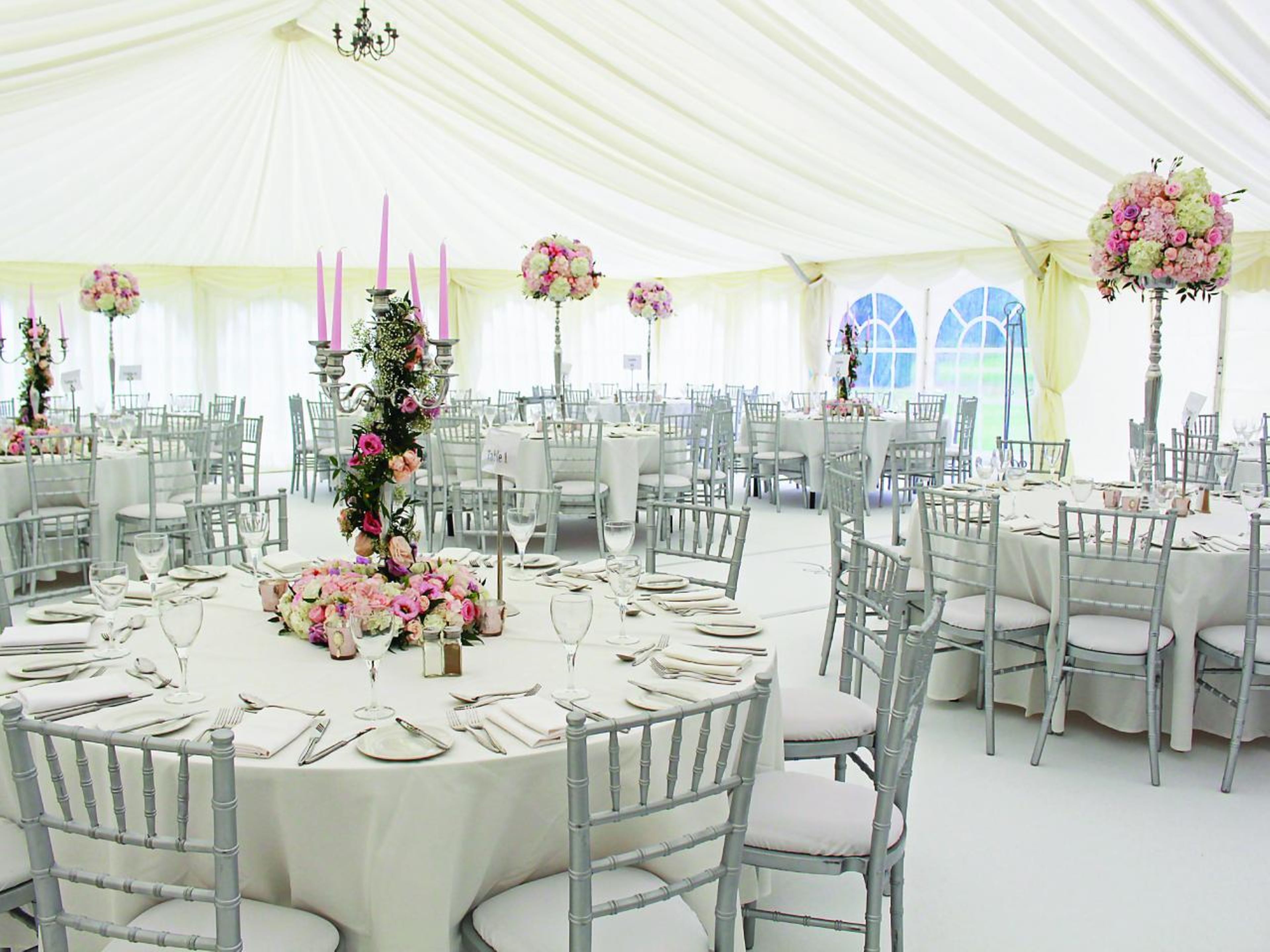 A tented event space with round tables, white tablecloths, and floral centerpieces.