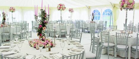 Un espacio para eventos con carpas, mesas redondas, manteles blancos y centros de mesa florales.