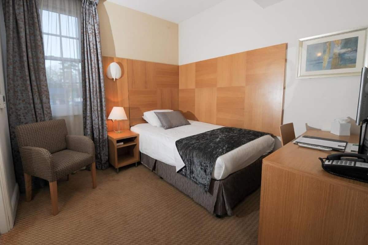 Une chambre d’hôtel avec un lit, un bureau, une chaise, une lampe et un tableau au mur.