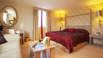 A hotel room with a bed, a desk with a lamp, a chair, a bedside table with a magazine, and a large mirror.