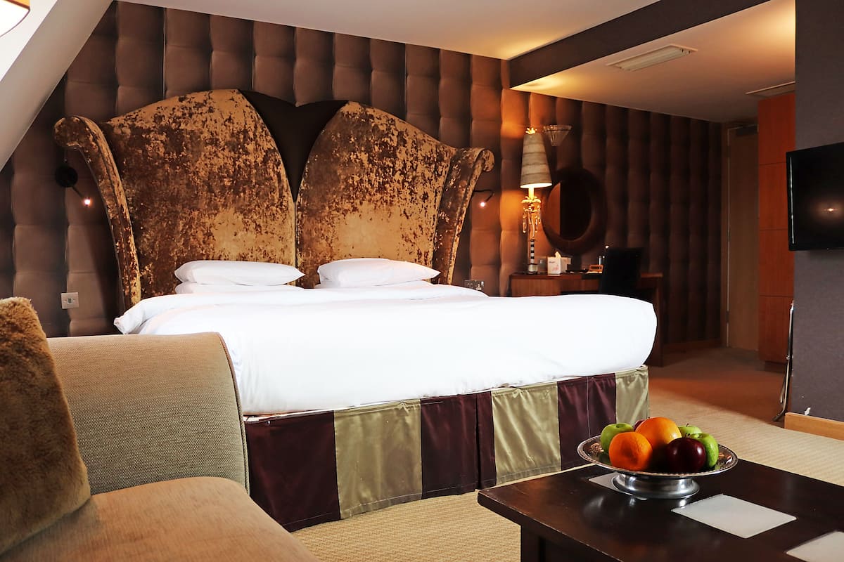 Une chambre d’hôtel avec un grand lit, une table de chevet sur laquelle se trouve un panier de fruits, et un téléviseur fixé au mur.