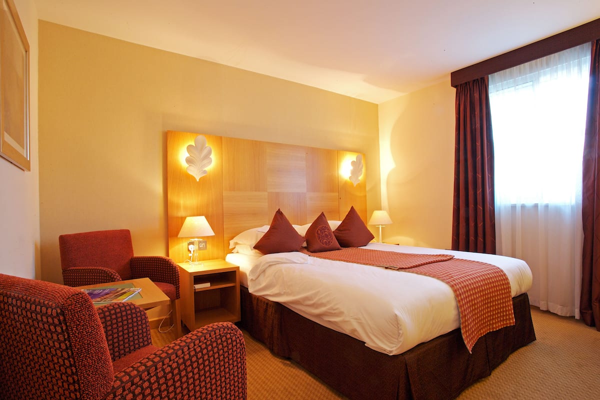 Une chambre d’hôtel avec un grand lit, deux tables de chevet avec des lampes, un canapé rouge à motifs et une petite table avec un magazine.