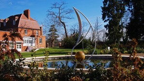 Ein Innenhof mit einem Brunnen, einem roten Backsteinhaus und einer Skulptur.