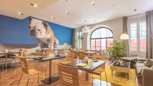 A modern dining area with wooden chairs and tables, a large wall mural of a bulldog, and large windows with curtains. - Urban Style Bordeaux Centre Hotel de la Presse (Bordeaux)