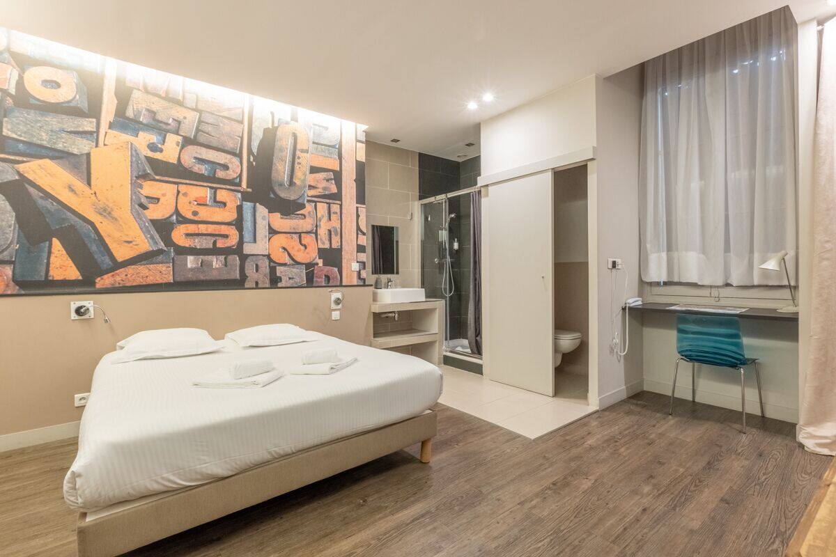 Una habitación de hotel moderna con una cama grande, zona de ducha, escritorio y baño.