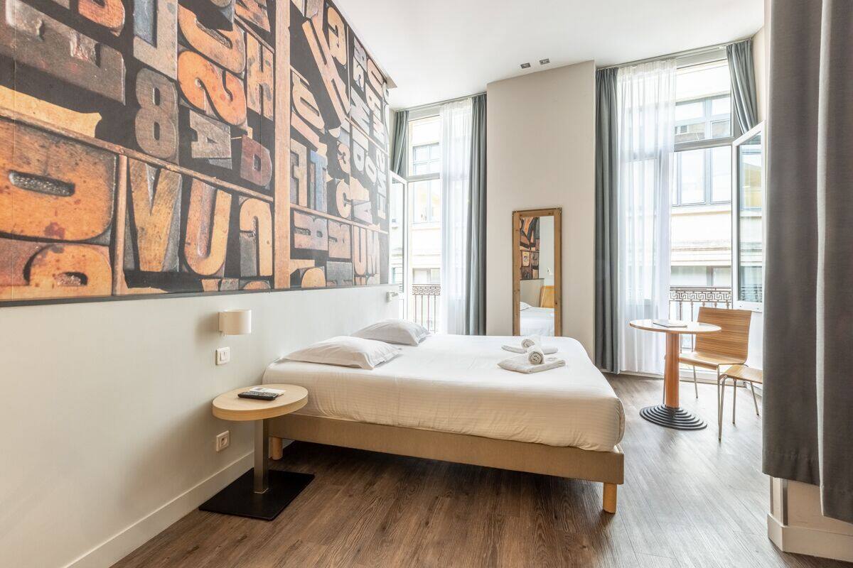 Habitación de hotel con una cama grande, una mesita redonda pequeña, una silla y un cuadro abstracto grande en la pared.