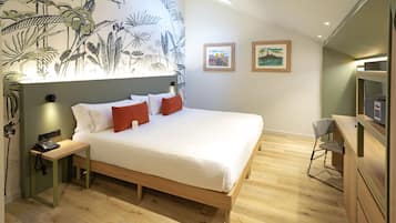 A modern hotel room with a large bed, a desk, and a chair. There are two framed pictures on the wall.