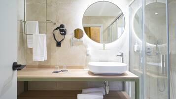 A modern bathroom with a large round mirror, a white sink, and a glass-enclosed shower.
