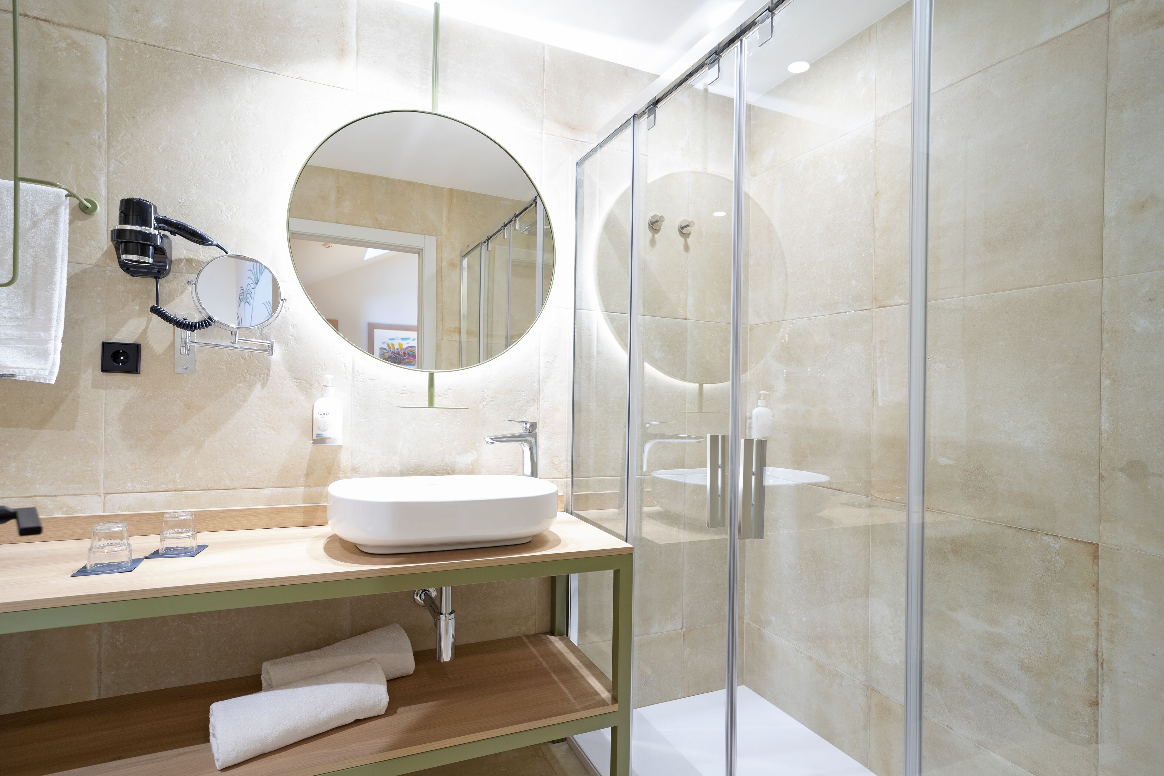 A modern bathroom with a large round mirror, a white sink, and a glass shower enclosure.