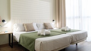 Habitación de hotel con dos camas, un cabecero grande, lámparas de noche y vistas al exterior.
