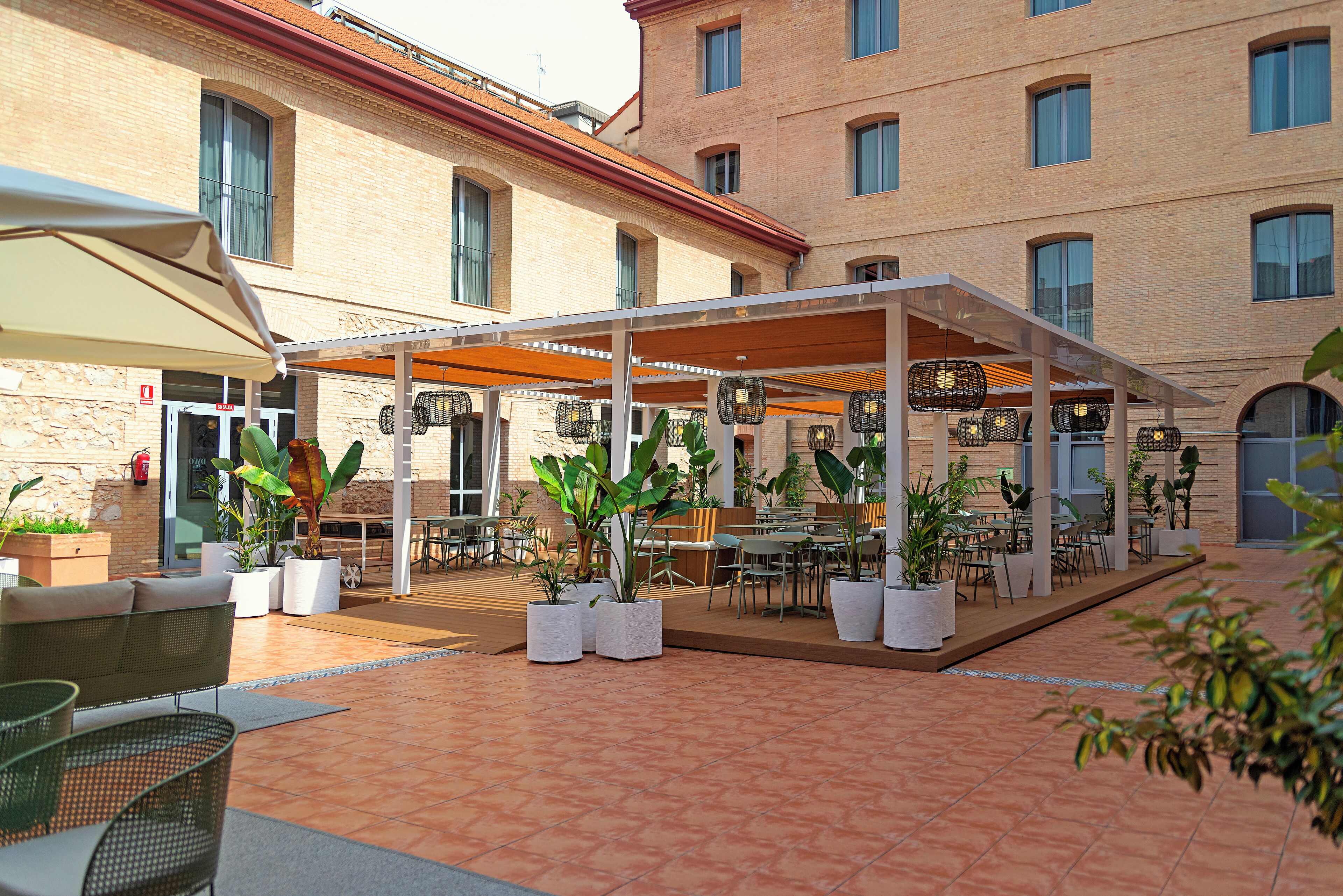 An outdoor patio area with tables and chairs, potted plants, and a covered seating area.