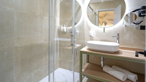 Un baño moderno con ducha envuelta en vidrio, espejo redondo y tocador de madera con lavamanos.