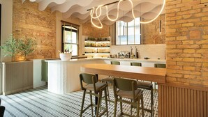Un área de bar moderna con una barra de madera, taburetes verdes y una pared de ladrillo.