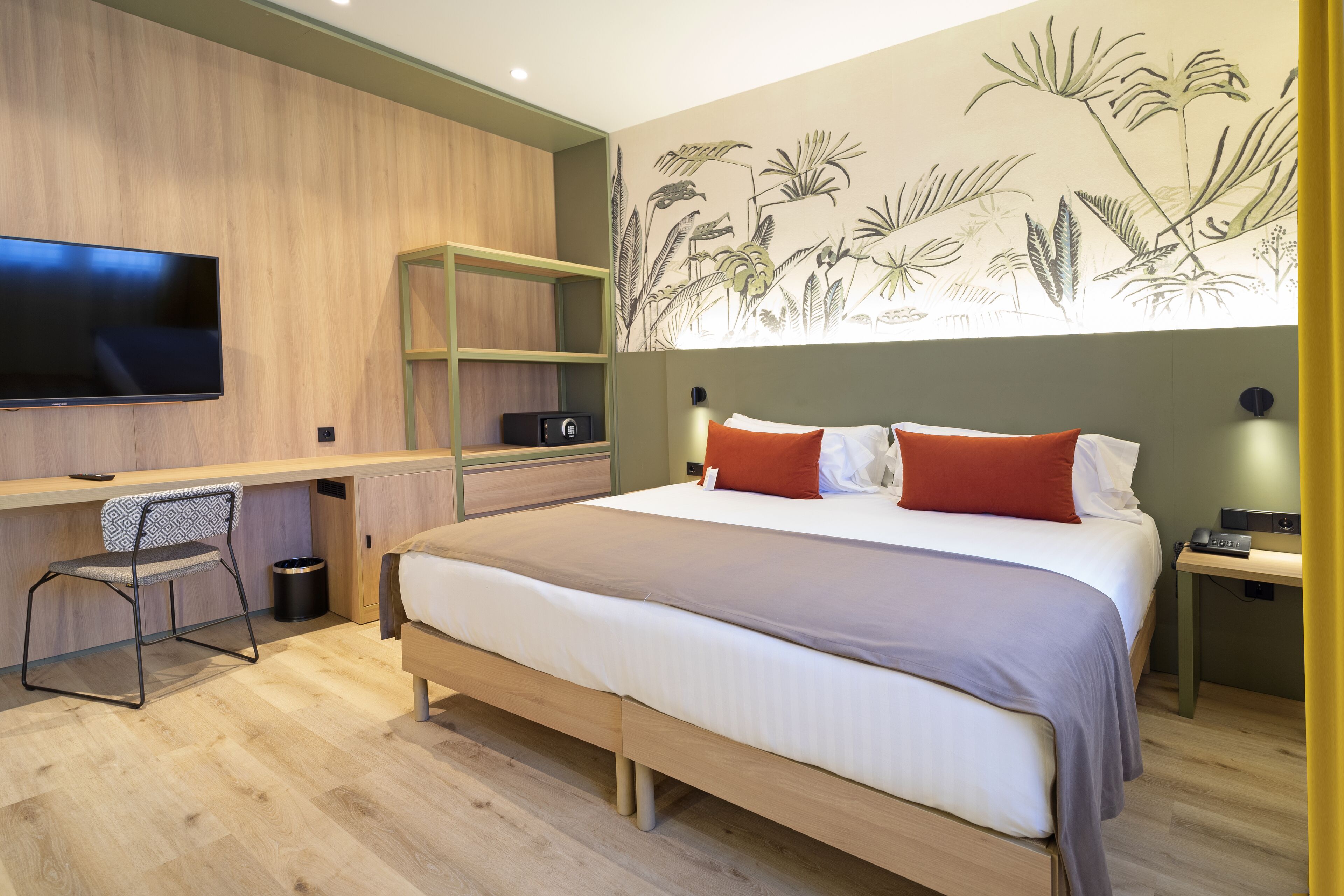 Una habitación de hotel moderna con una cama grande, un escritorio con una silla, un televisor de pantalla plana y un mural en la pared.