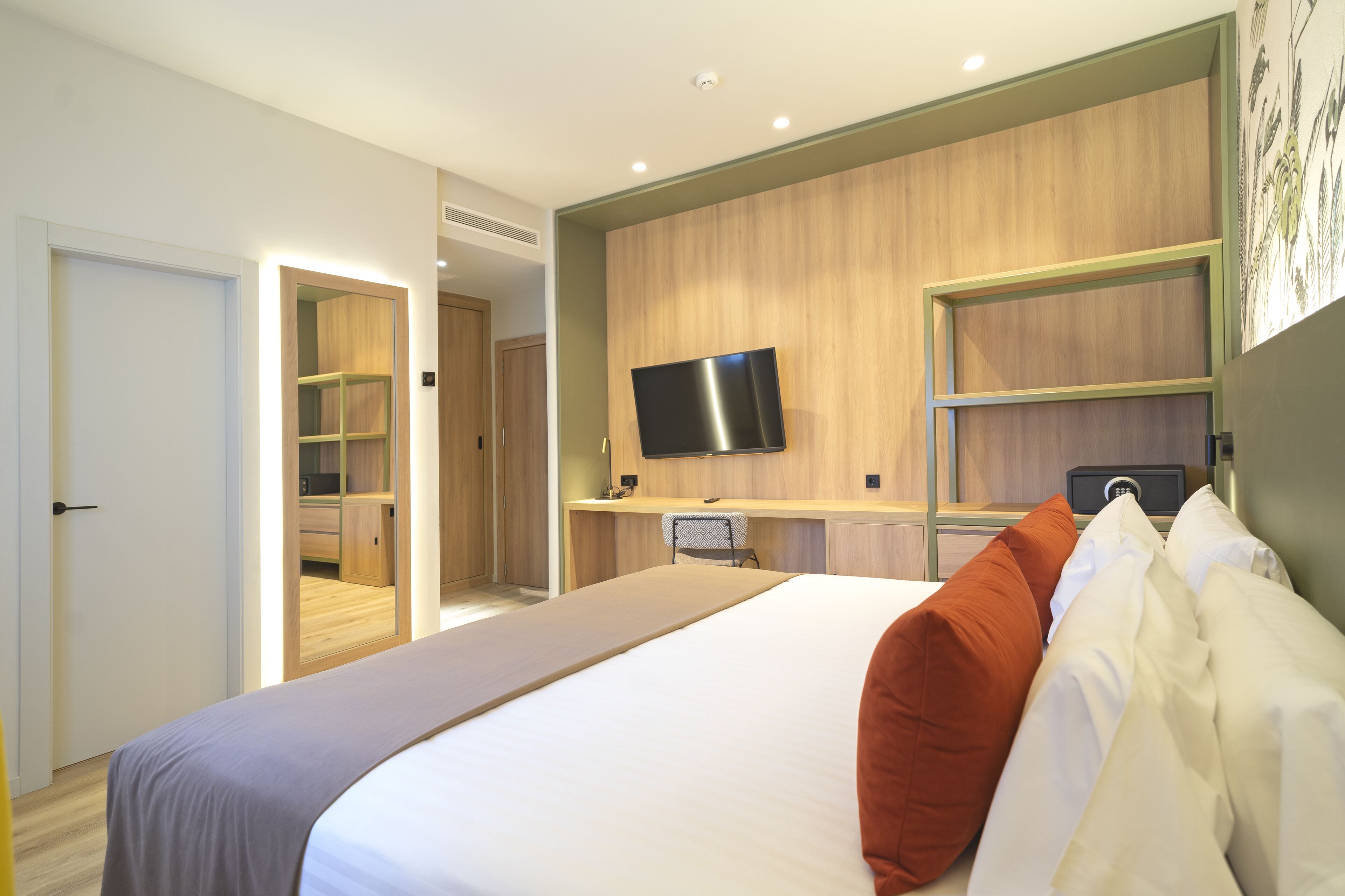 Una habitación de hotel moderna con una cama grande, un escritorio con televisor de pantalla plana y un vestidor.