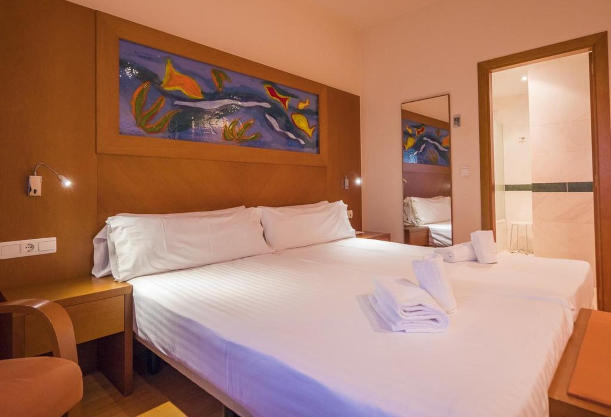 A hotel room with a large bed, a nightstand, a chair, a painting on the wall, and a mirror.