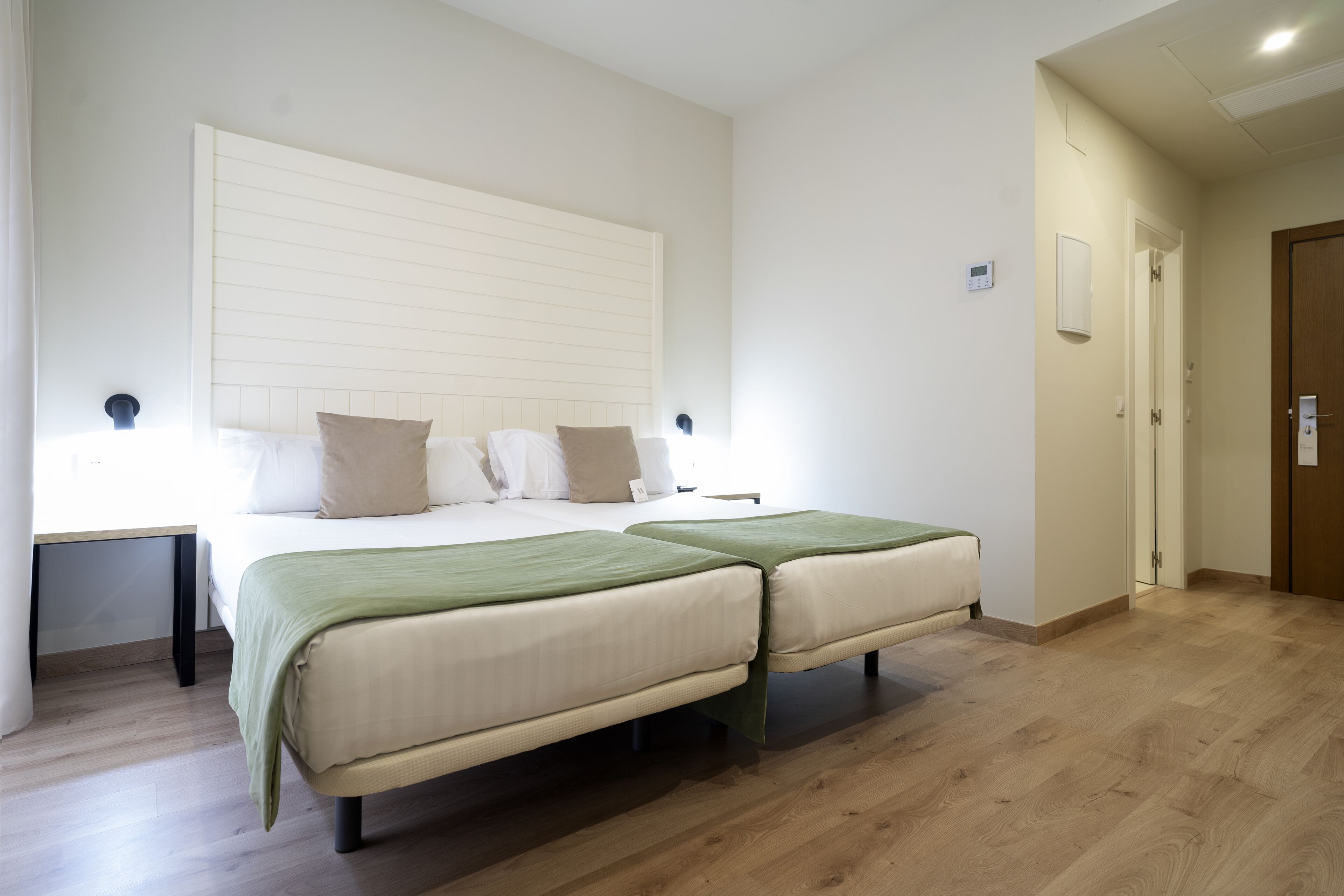 A bedroom with two beds, a bedside table, a nightstand, a wooden floor, and a door.
