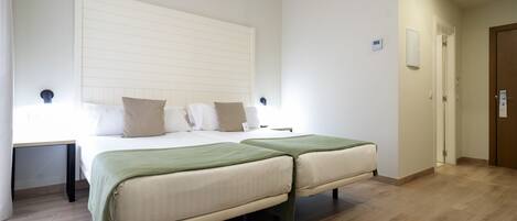 A bedroom with two beds, a bedside table, a nightstand, a wooden floor, and a door.