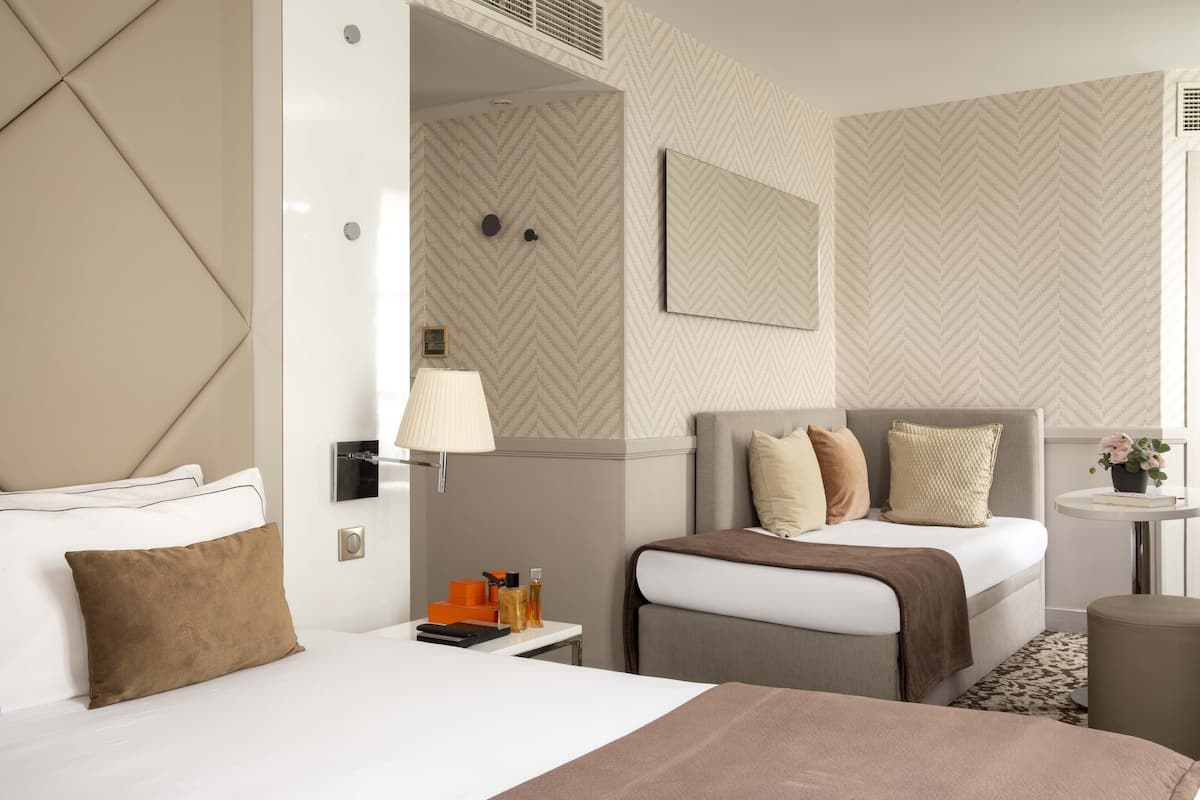 A hotel room with two beds, a bedside table with a lamp, a small table with a plant, and a mirror on the wall.