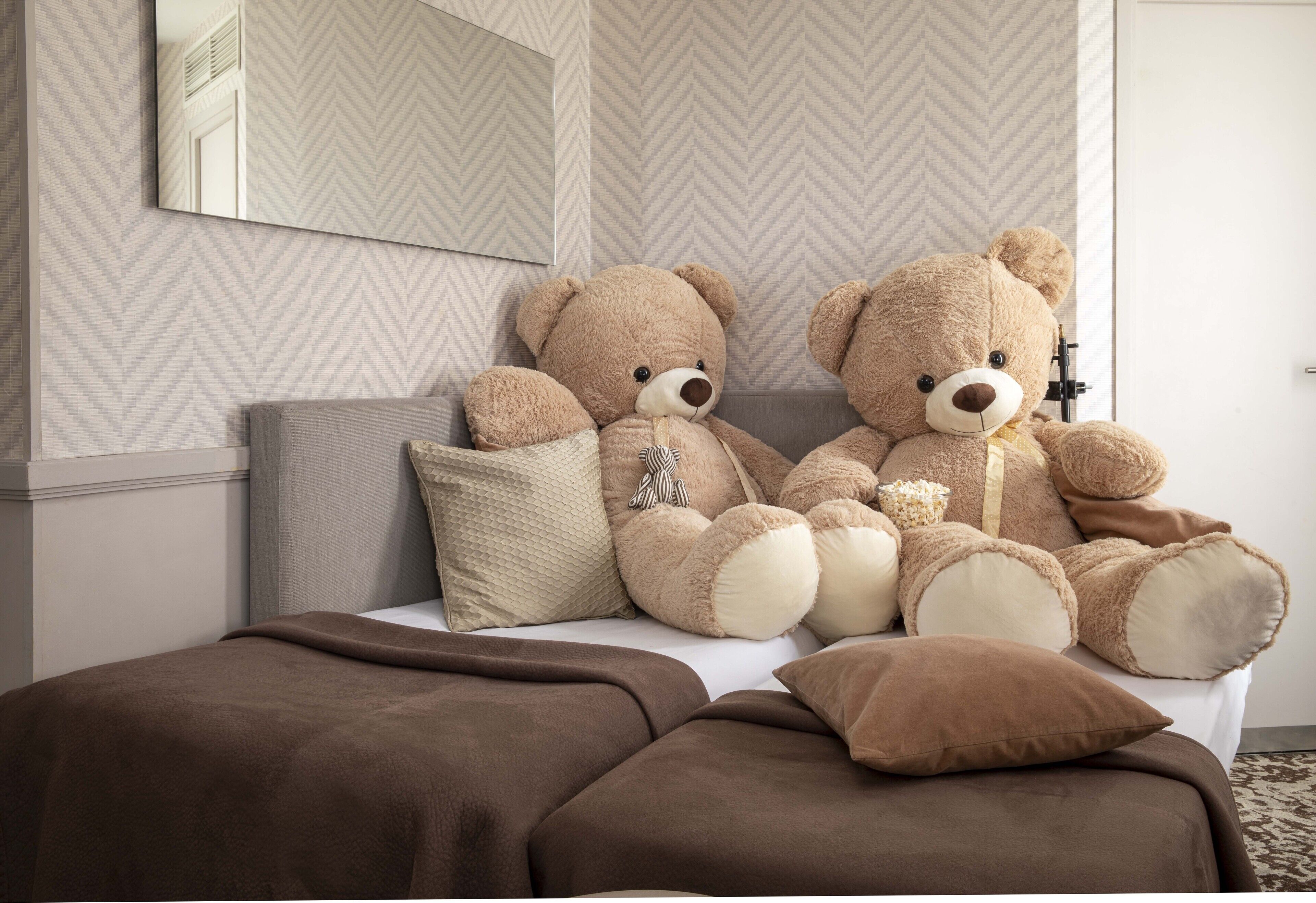 A bed with two large teddy bears, a pillow, and a blanket.