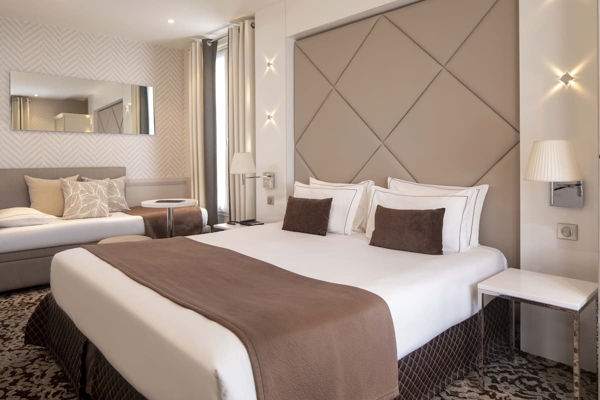 A hotel room with a large bed, a smaller bed, a bedside table, a nightstand, a mirror, and a patterned carpet.
