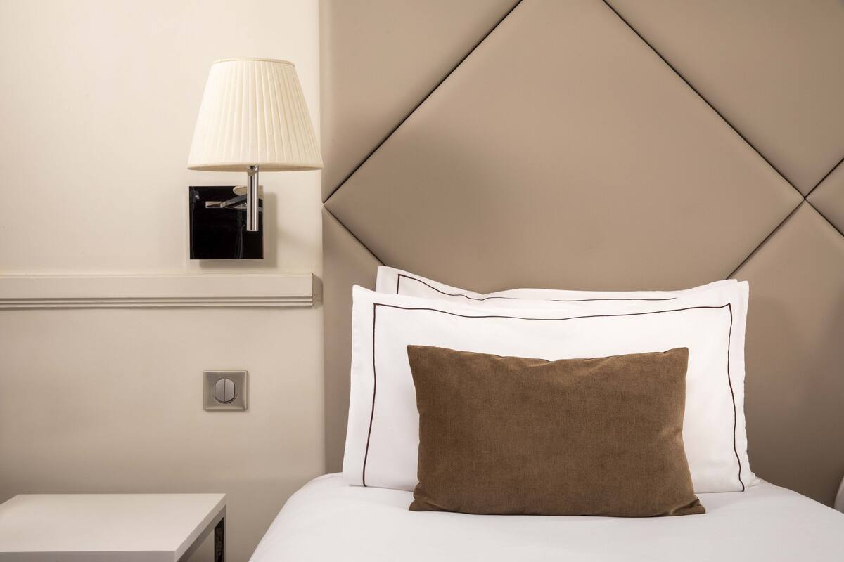 A neatly made bed with a brown pillow, a bedside lamp, and a wall-mounted light fixture.