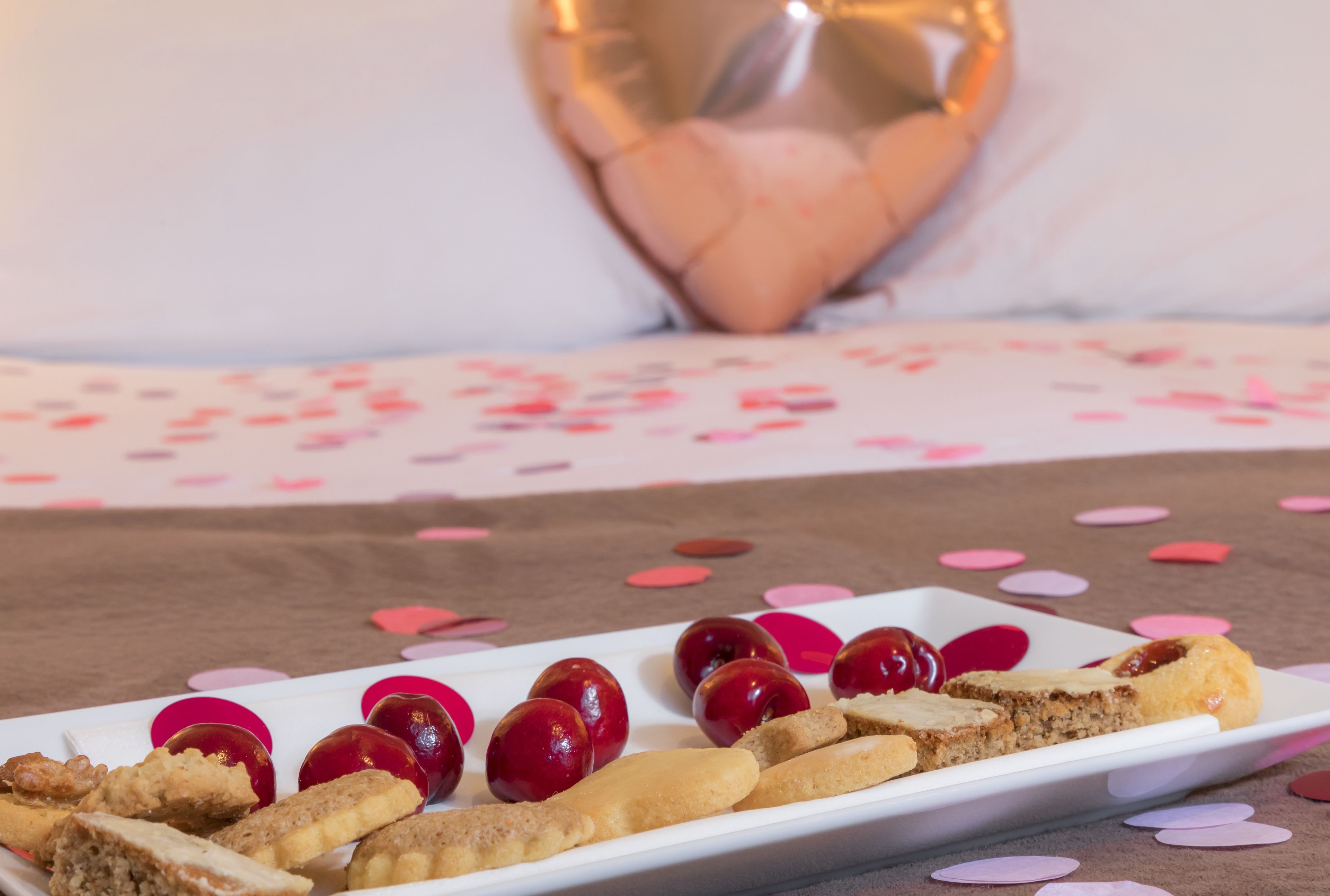 A white rectangular plate with cherry tomatoes and breadsticks on a table with scattered pink heart-shaped confetti.