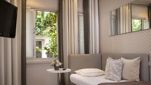 Una habitación de hotel moderna con una cama, una mesita de noche con un florero y una televisión montada en la pared, además de un ventanal con cortinas.
