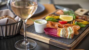 A dining table with a glass of white wine, a wooden board with various foods, and a small bowl of sauce.
