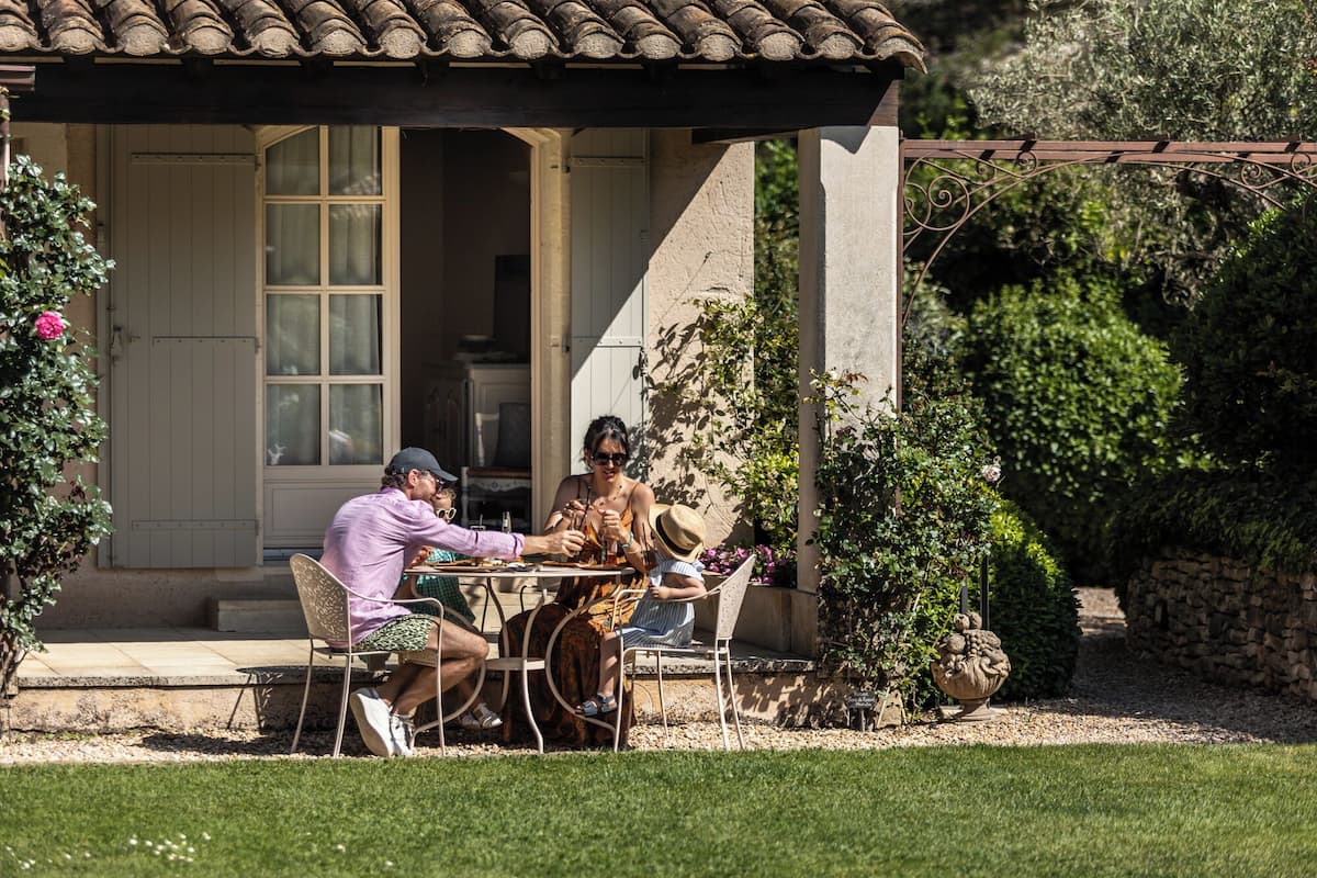 Une terrasse avec une table et des chaises, un mur en pierre et un jardin agrémenté de différentes plantes.