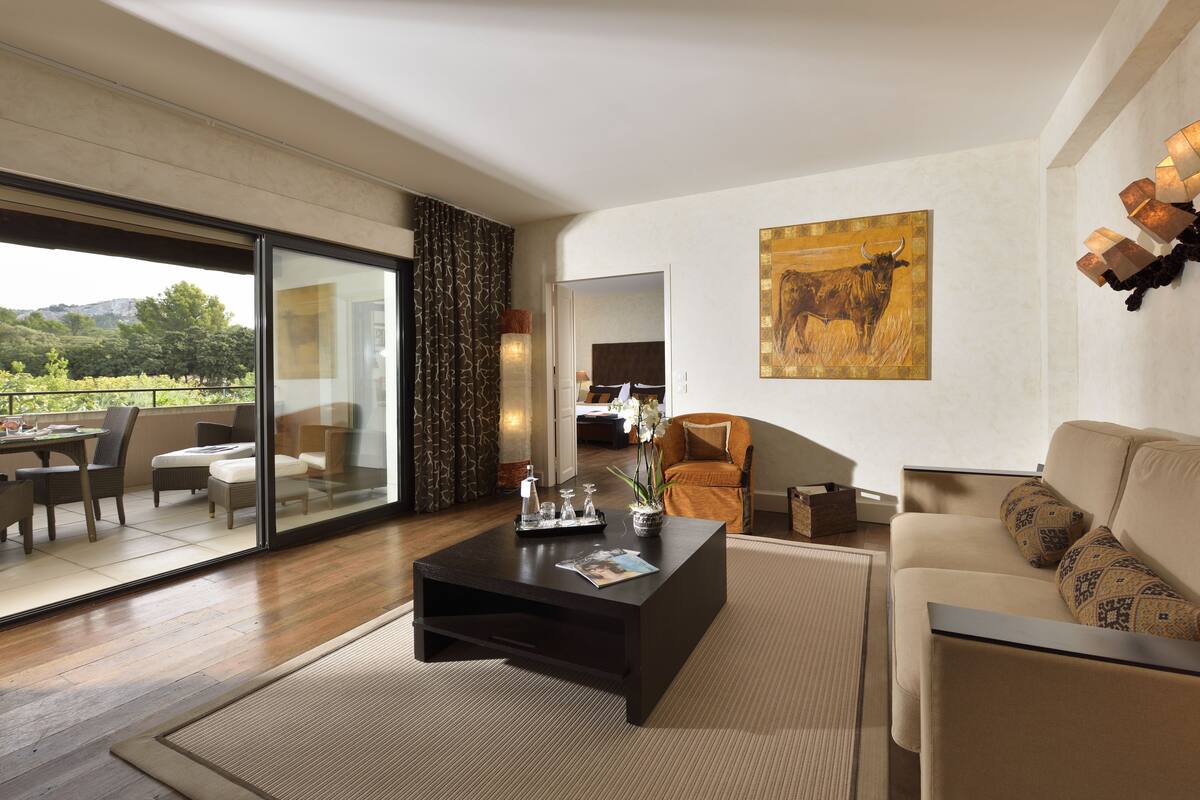 Un salon moderne avec une porte vitrée donnant sur une terrasse extérieure, une table basse de couleur sombre, un canapé beige et un grand tableau accroché au mur.