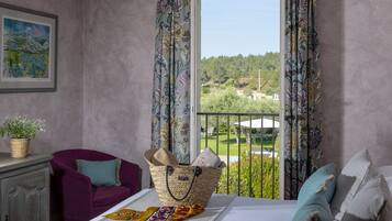 Una habitación con una cama, un sillón morado, una cesta de mimbre y vistas a un paisaje verde por la ventana.